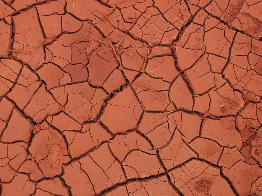 Solo argiloso seco com rachaduras profundas mostrando baixa permeabilidade e retração da argila